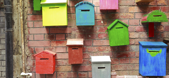 Pink, green, white, red, and blue bird houses hanging on a red brick wall outside